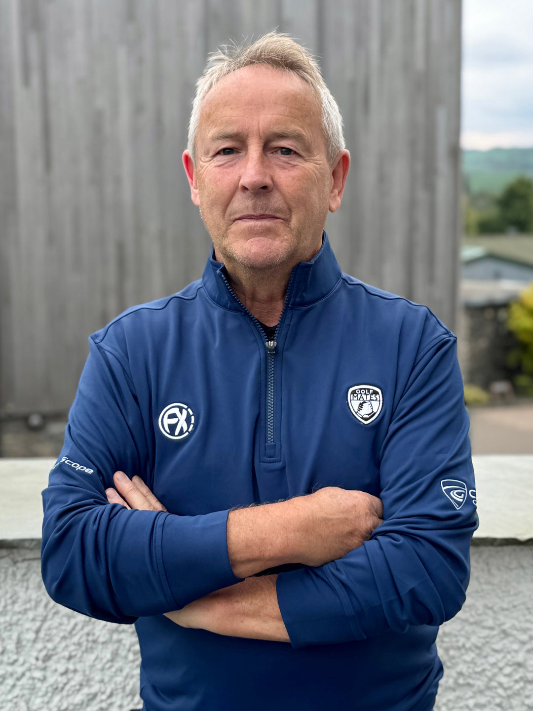 Man wearing a blue golf jacket with logos standing outdoors.